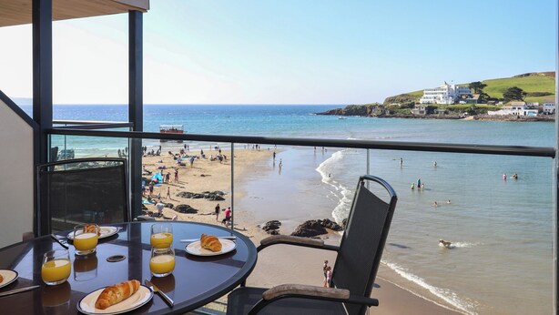 A balcony with a table set for breakfast, overlooking a beach with people and a boat in the distance. - 14 Burgh Island Causeway (Kingsbridge)
