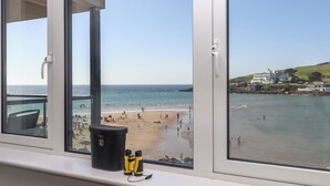 A window with binoculars and a bucket on the ledge, overlooking a beach with people and a building in the background. - 14 Burgh Island Causeway (Kingsbridge)
