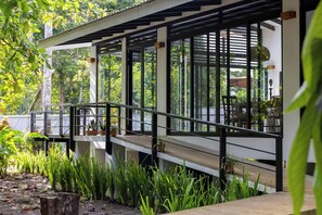 A covered outdoor area with a railing, potted plants, and a view of greenery.