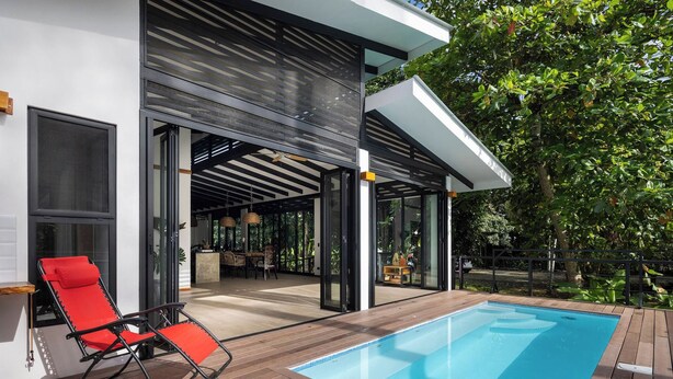 A modern outdoor pool area with a red lounge chair, a covered patio, and a view of the interior. - Casa Kali - 4-Min Walk to Beach - AC & Pool (Puerto Viejo de Talamanca)