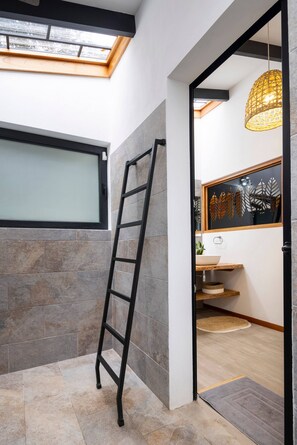 A modern bathroom with a skylight, a ladder, and a decorative wall panel.
