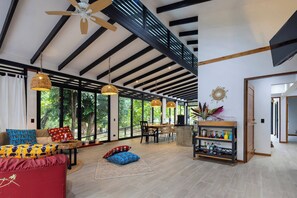 A spacious living area with a high ceiling, large windows, and a dining area.