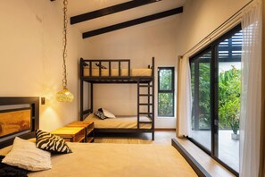 A room with a bunk bed, a desk, a hanging light fixture, and a large window with a view of greenery.