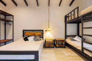 A room with bunk beds, a bedside table, a hanging light fixture, and a wall-mounted shelf.