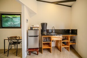 A compact kitchen with a refrigerator, coffee maker, sink, and wooden shelves.