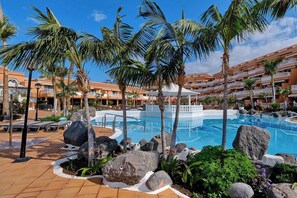 A resort pool area with palm trees, a central pool, and a building with balconies. - Home2Book Modern Design Seaview Apt, Pool&Terrace (Playa de la Américas)