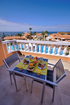 A table set with breakfast items on a balcony overlooking a pool and ocean view.