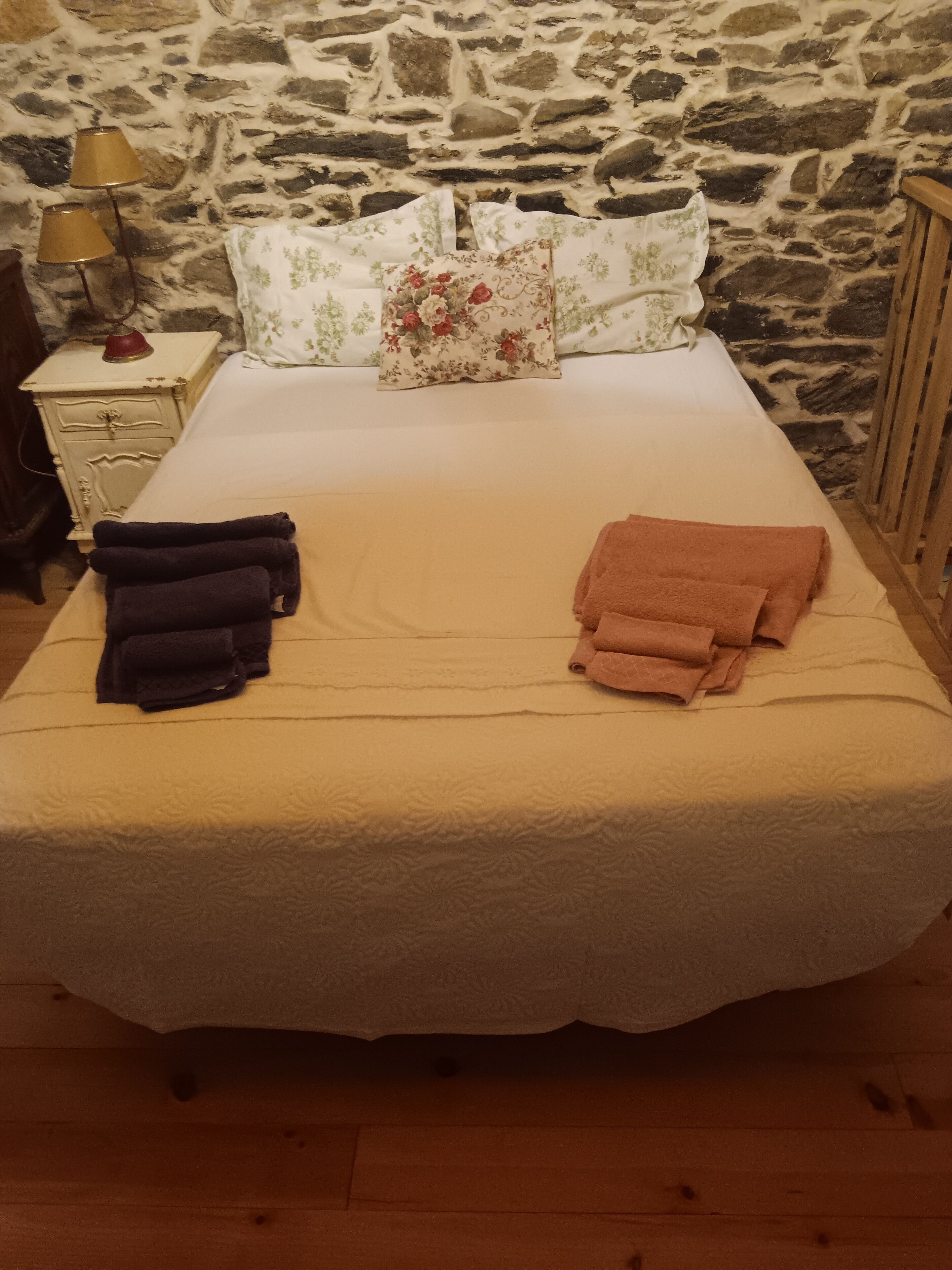 Ein Bett mit weißer Bettdecke, zwei Kissen mit Blumenmuster und zwei gefaltete Handtücher.