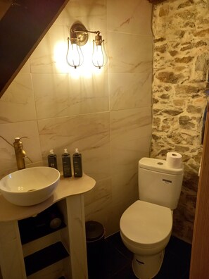 Ein Badezimmer mit einem weißen Waschbecken, zwei Lampen, einer Toilette und Pflegeartikeln auf der Ablagefläche.