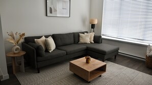 Ein modernes Wohnzimmer mit einer Eckcouch, einem Holztisch, einem Beistelltisch mit Vase und einer Stehlampe.