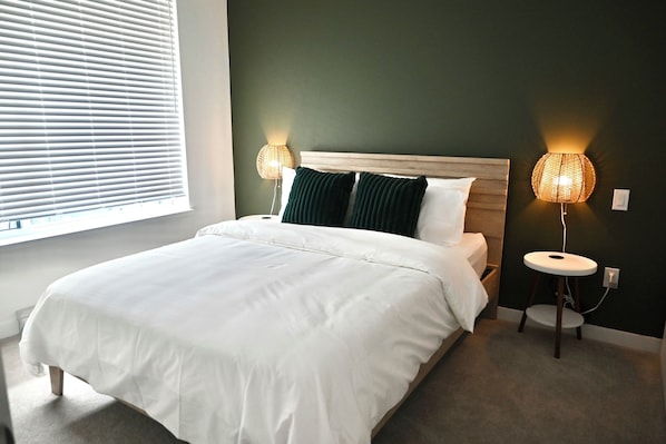 Cama bem arrumada com lençóis brancos, duas luminárias de cabeceira e uma janela com persianas.