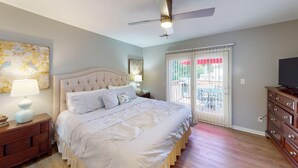 Une chambre avec un grand lit, un ventilateur de plafond, un téléviseur posé sur une commode et une vue sur l’extérieur grâce à une porte coulissante.