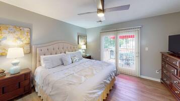 A bedroom with a large bed, a ceiling fan, a TV on a dresser, and a view of the outside through a sliding door.