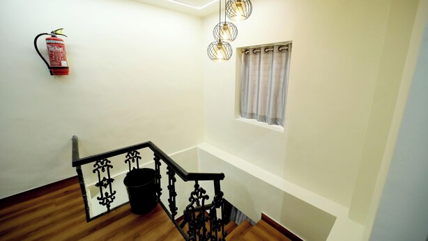 A staircase with a black railing, a fire extinguisher on the wall, and a window with curtains. - CABINSTAY MAROL- THE HUBZ (Mumbai)