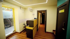 A reception area with a desk, a chair, a fan, and a sign indicating a kitchen. - CABINSTAY MAROL- THE HUBZ (Mumbai)