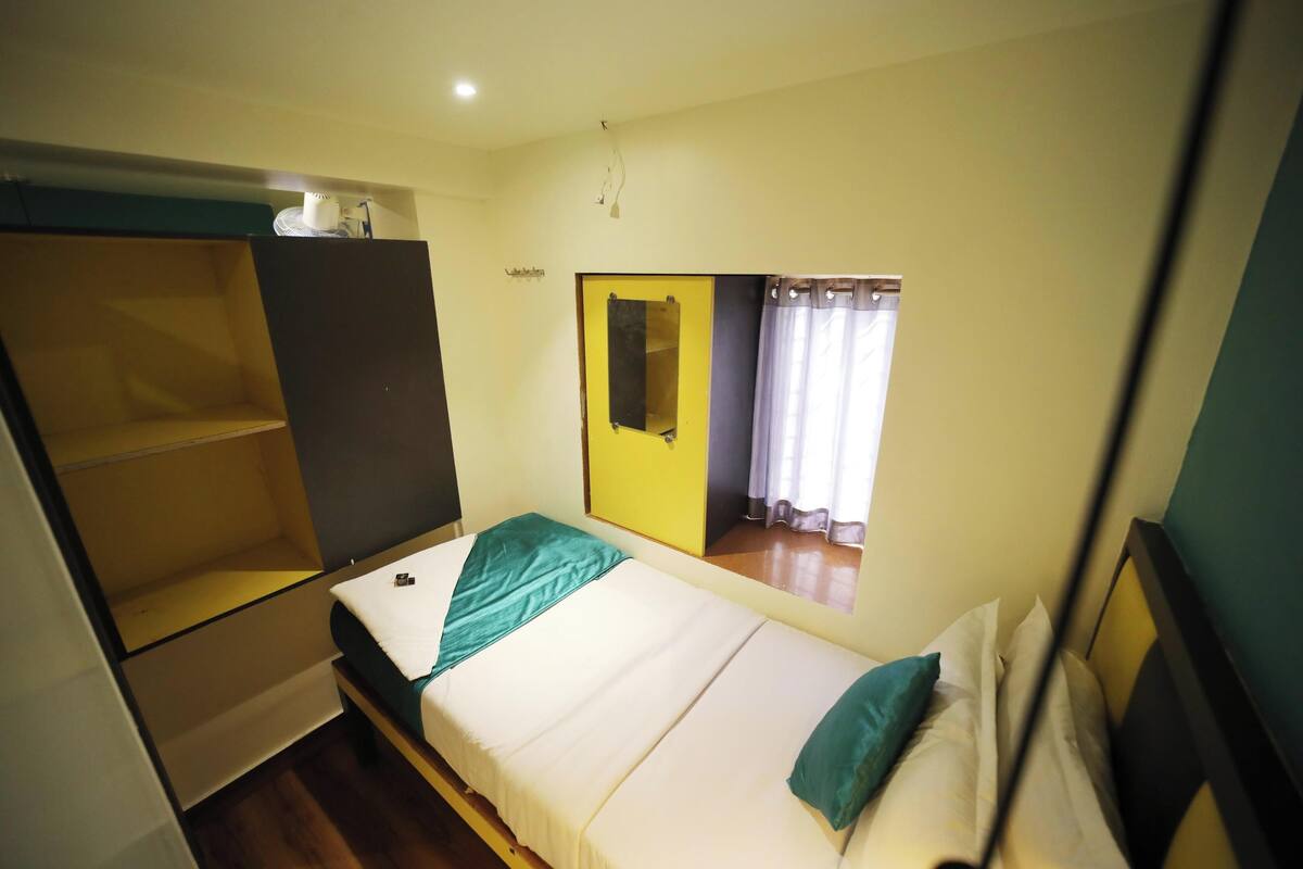 Un dormitorio con cama, armario, espejo y ventana con cortinas.