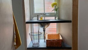 Ett litet köksutrymme med ett fönster, en diskho, en korg och en vas med blommor.