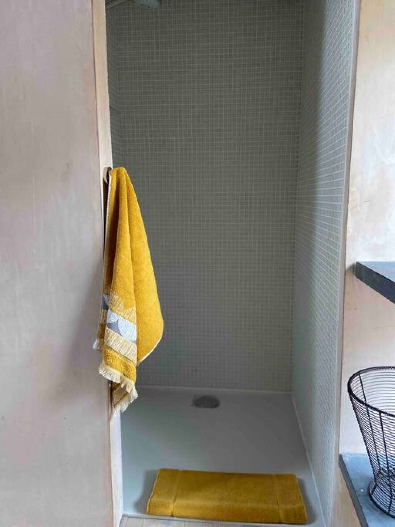 Un espacio de ducha pequeño y cerrado, con una toalla amarilla colgada en la pared y un perchero metálico a la derecha.