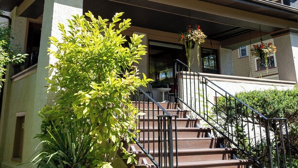 Une maison à deux étages avec un porche à l’avant, un escalier et un petit jardin.