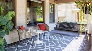 Un patio couvert doté d’un sol à motifs, de deux chaises à motifs avec des coussins rouges, d’une petite table ronde et d’une plante suspendue.