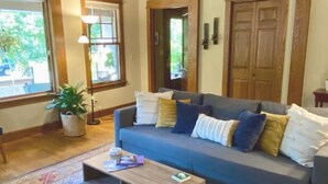 Un salon avec un canapé bleu, des poutres en bois, une grande fenêtre et une porte.