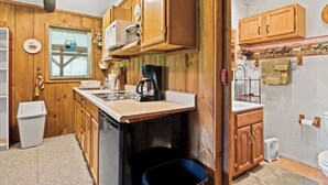 Une cuisine compacte avec des meubles de rangement en bois, un petit plan de travail, une machine à café et une poubelle.