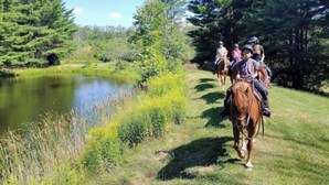 Un groupe de personnes à cheval, qui se déplacent le long d’un sentier bordant un étang dans une zone boisée.