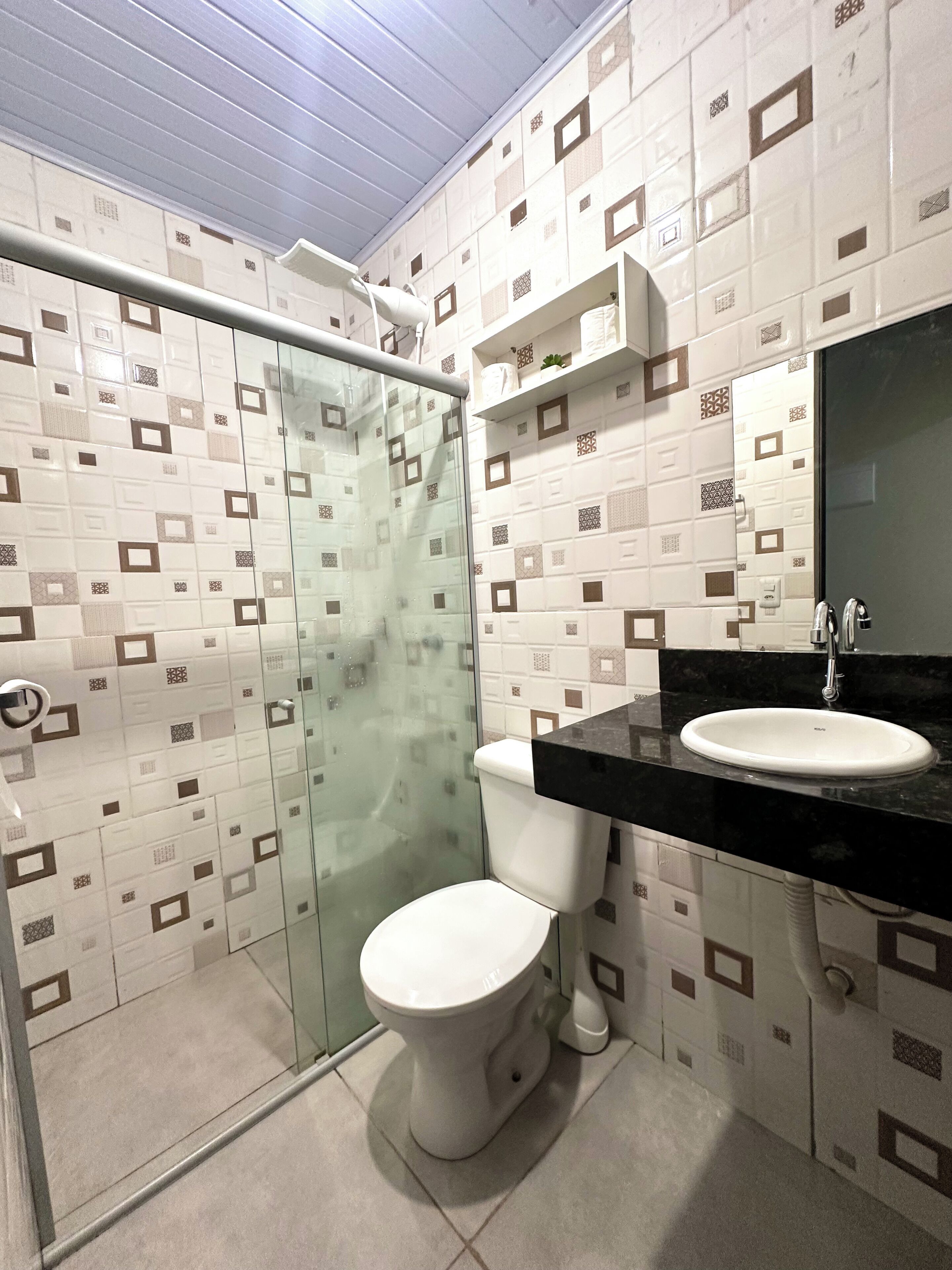 A bathroom with a toilet, a glass shower enclosure, a sink with a black countertop, and patterned tiles on the walls.