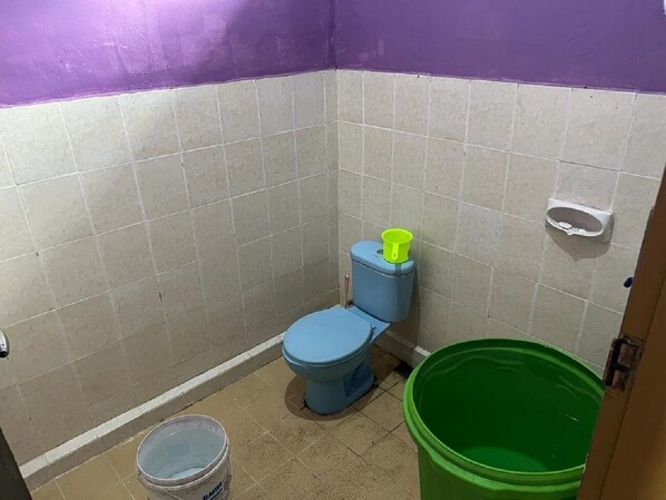 Un baño pequeño con un inodoro, un balde verde y un balde blanco.