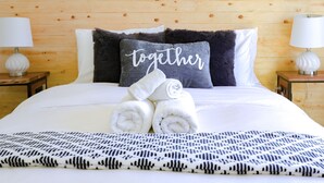 Un lit bien fait, avec des serviettes pliées, une couverture à motifs noir et blanc et un oreiller orné du mot « ensemble ».