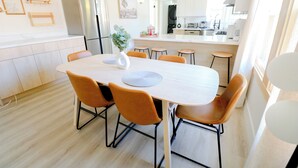 Une cuisine moderne dotée d’un îlot central, d’un coin repas avec une table ronde et des chaises orange, ainsi que d’un réfrigérateur.