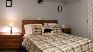 A bedroom with a bed, a nightstand, a lamp, and a wall with a framed picture. - Updated Main St Condo in downtown Ludlow! (Ludlow)