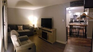 A living room with a sofa, a television, and a dining area with a table and chairs. - Updated Main St Condo in downtown Ludlow! (Ludlow)