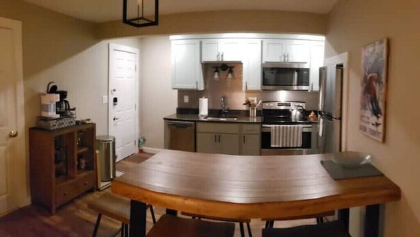 A modern kitchen with white cabinets, stainless steel appliances, and a wooden dining table with benches. - Updated Main St Condo in downtown Ludlow! (Ludlow)