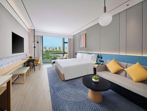 Una habitación de hotel moderna con una cama grande, un sofá, un comedor y vistas de la ciudad.