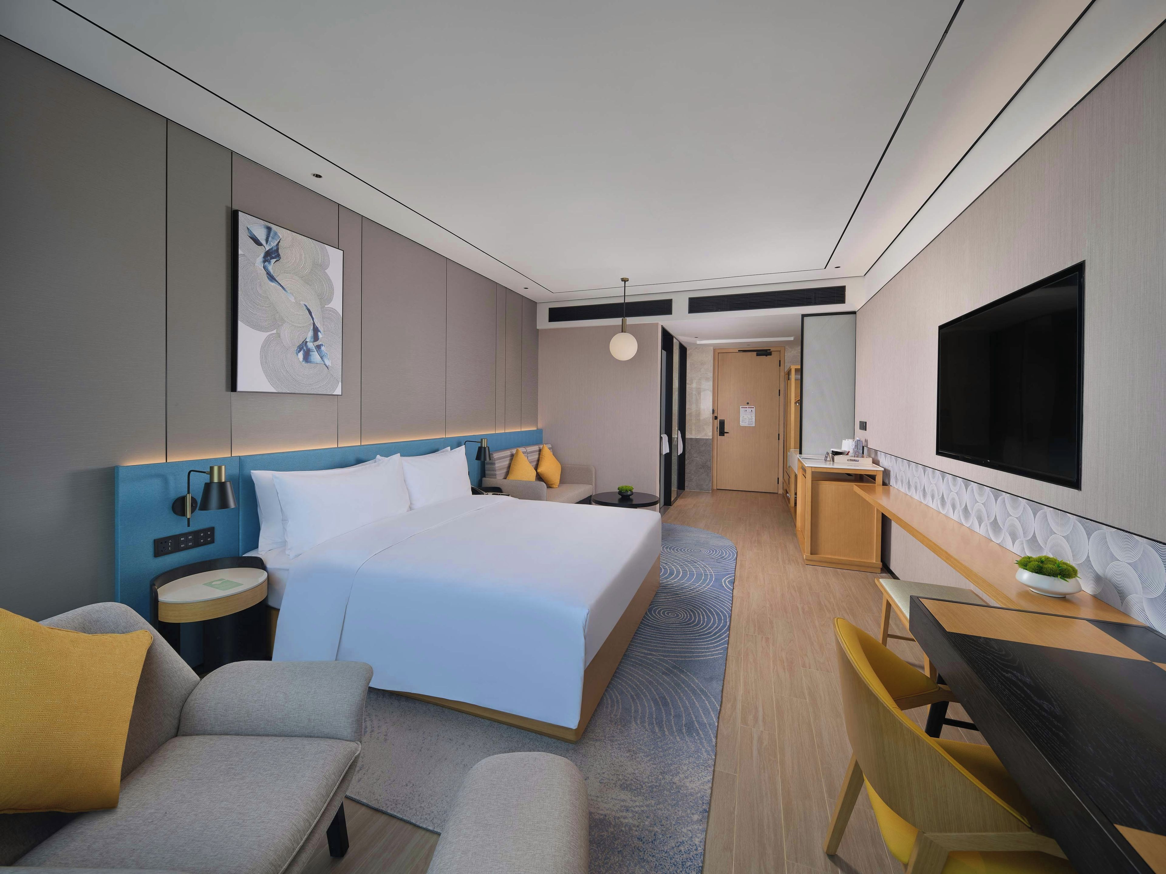 A modern hotel room with a large bed, bedside tables, a desk, and a TV.