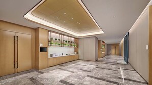 A modern hotel lobby with a long reception desk, wooden paneling, and a ceiling with recessed lighting. - Hilton Garden Inn Xiamen Tong'an (Xiamen)