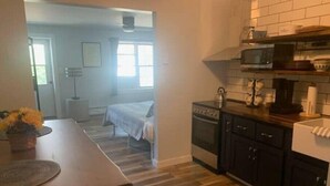 Une cuisine compacte avec un plan de travail en bois, une cuisinière et un four à micro-ondes. On y trouve une table à manger avec un banc et une plante en pot.