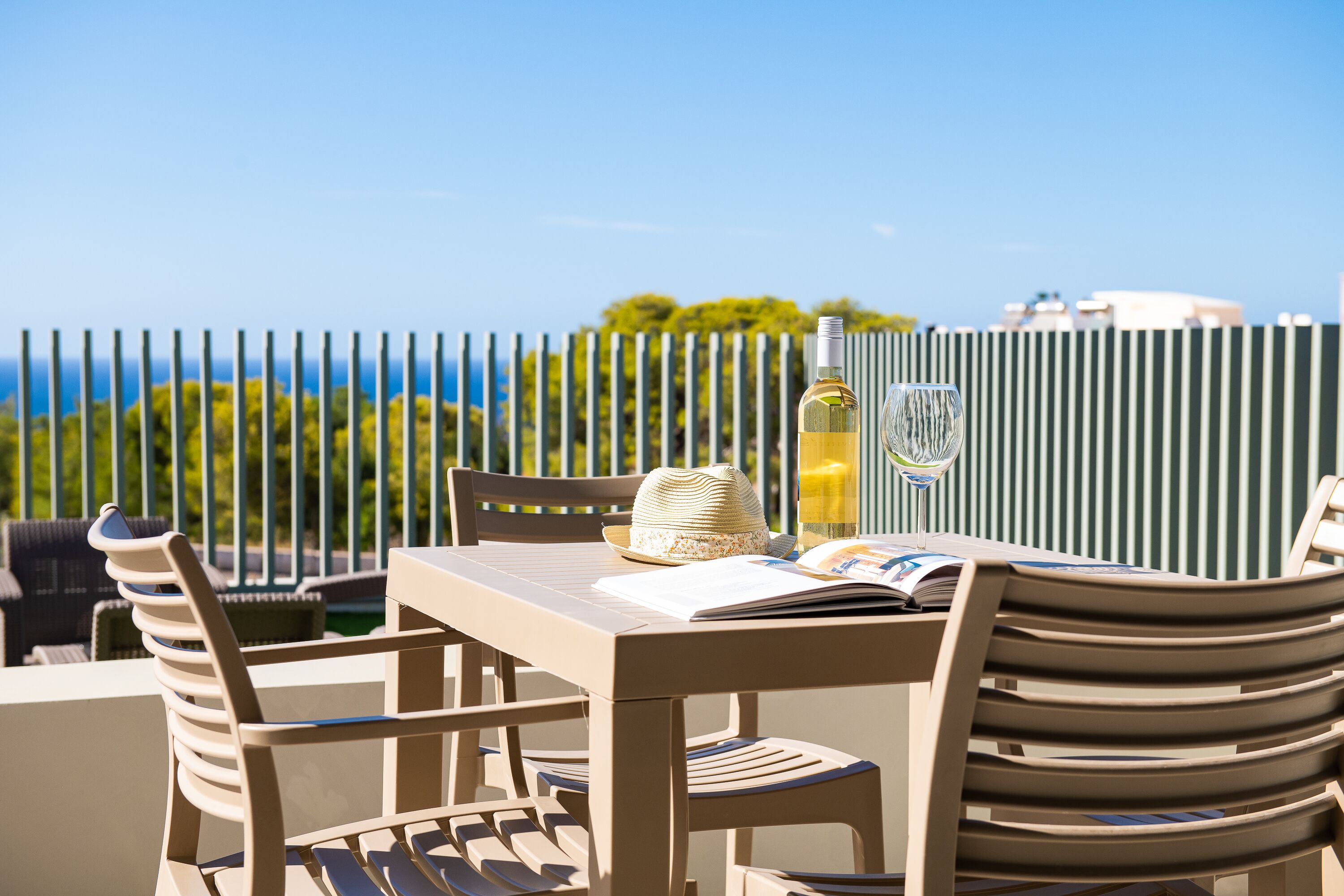 A terrace with a table set for two, a bottle of wine, and a hat.