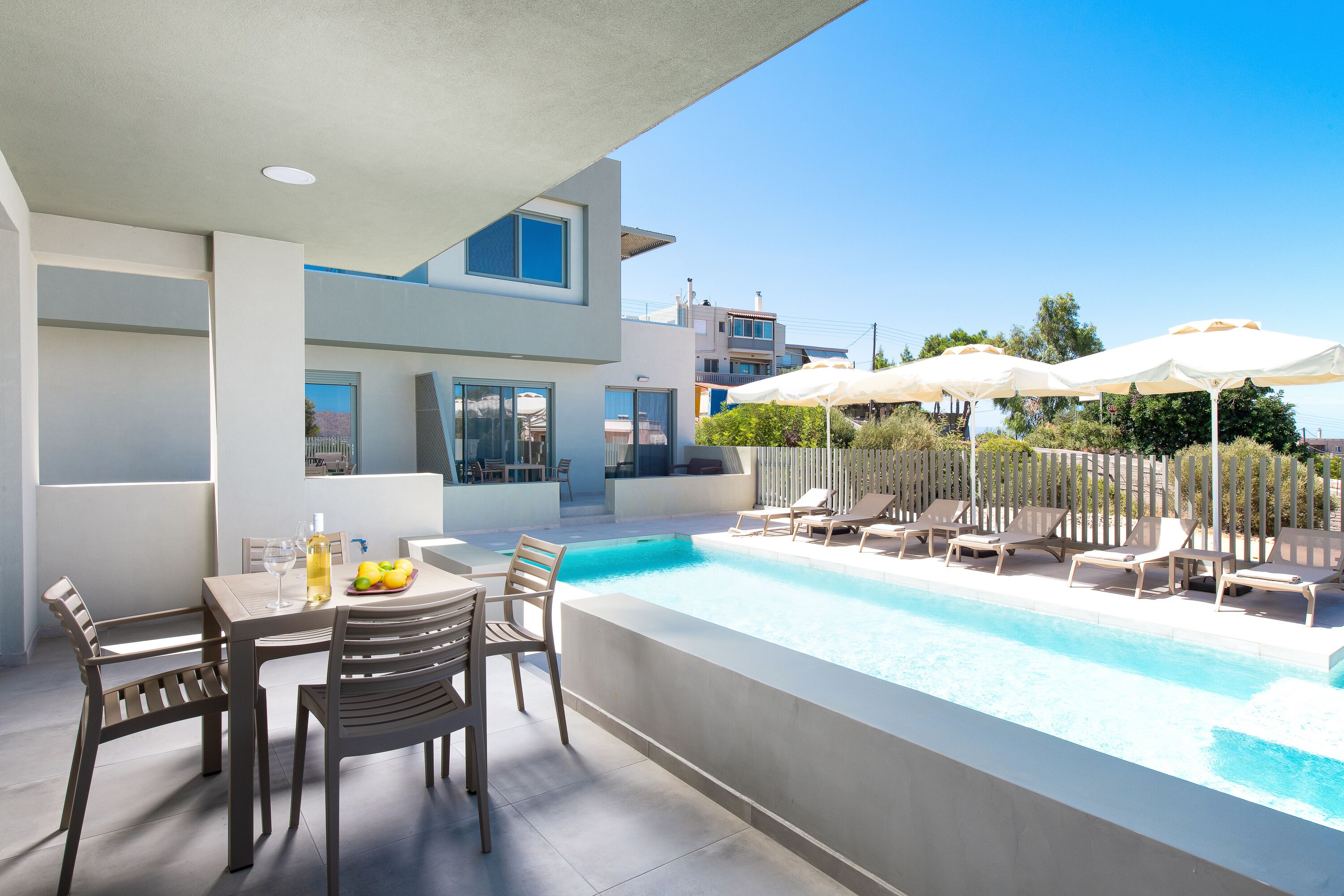 A modern outdoor pool area with lounge chairs and umbrellas, a dining table with chairs, and a clear view of the surrounding buildings.