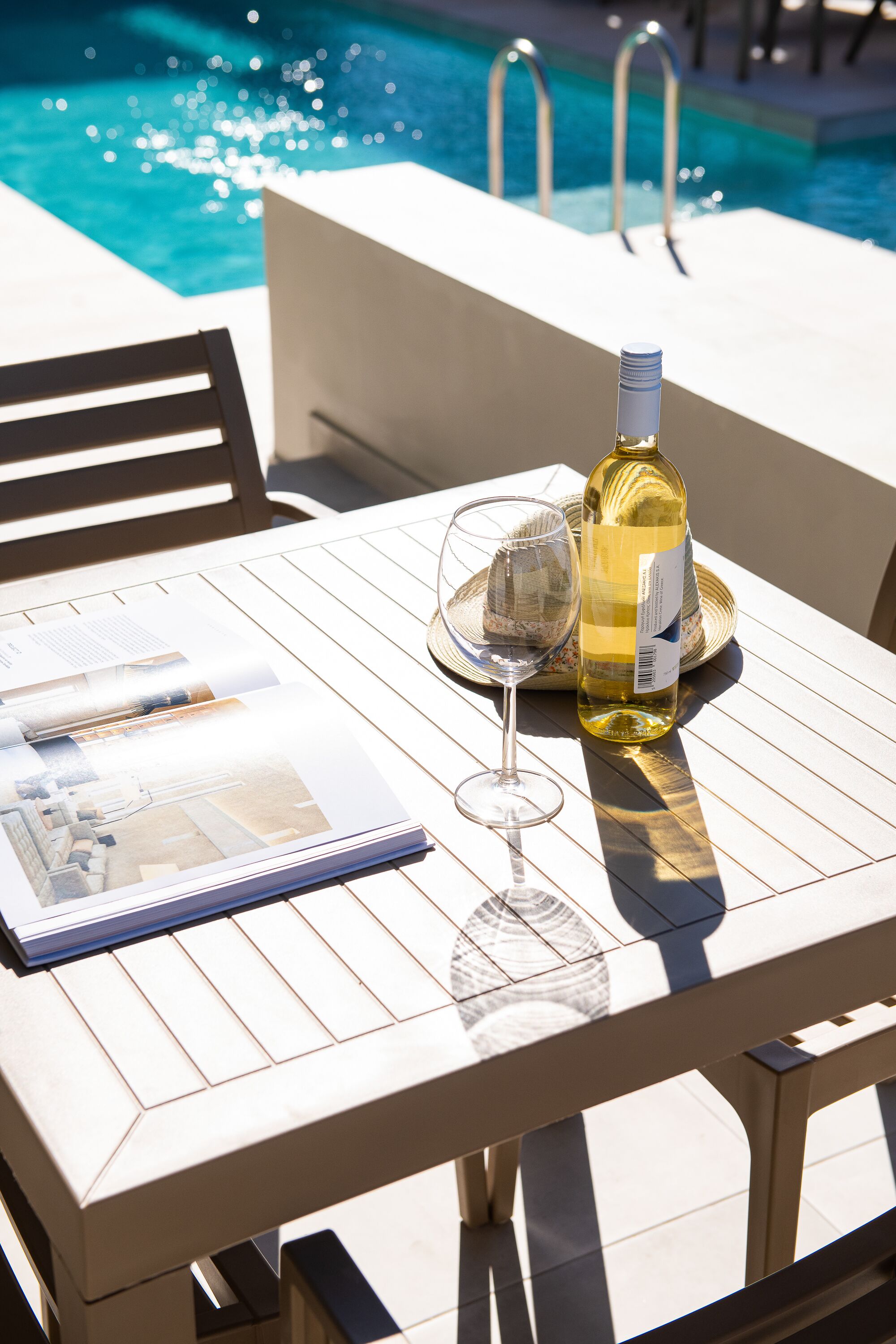 A poolside table with a wine bottle, a glass, and a menu.