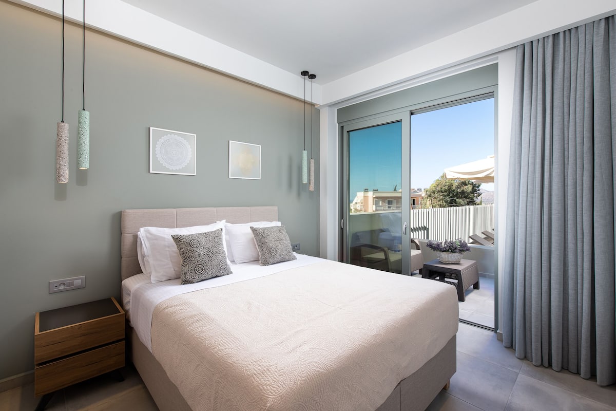 A modern bedroom with a large bed, bedside tables, and a balcony with curtains.