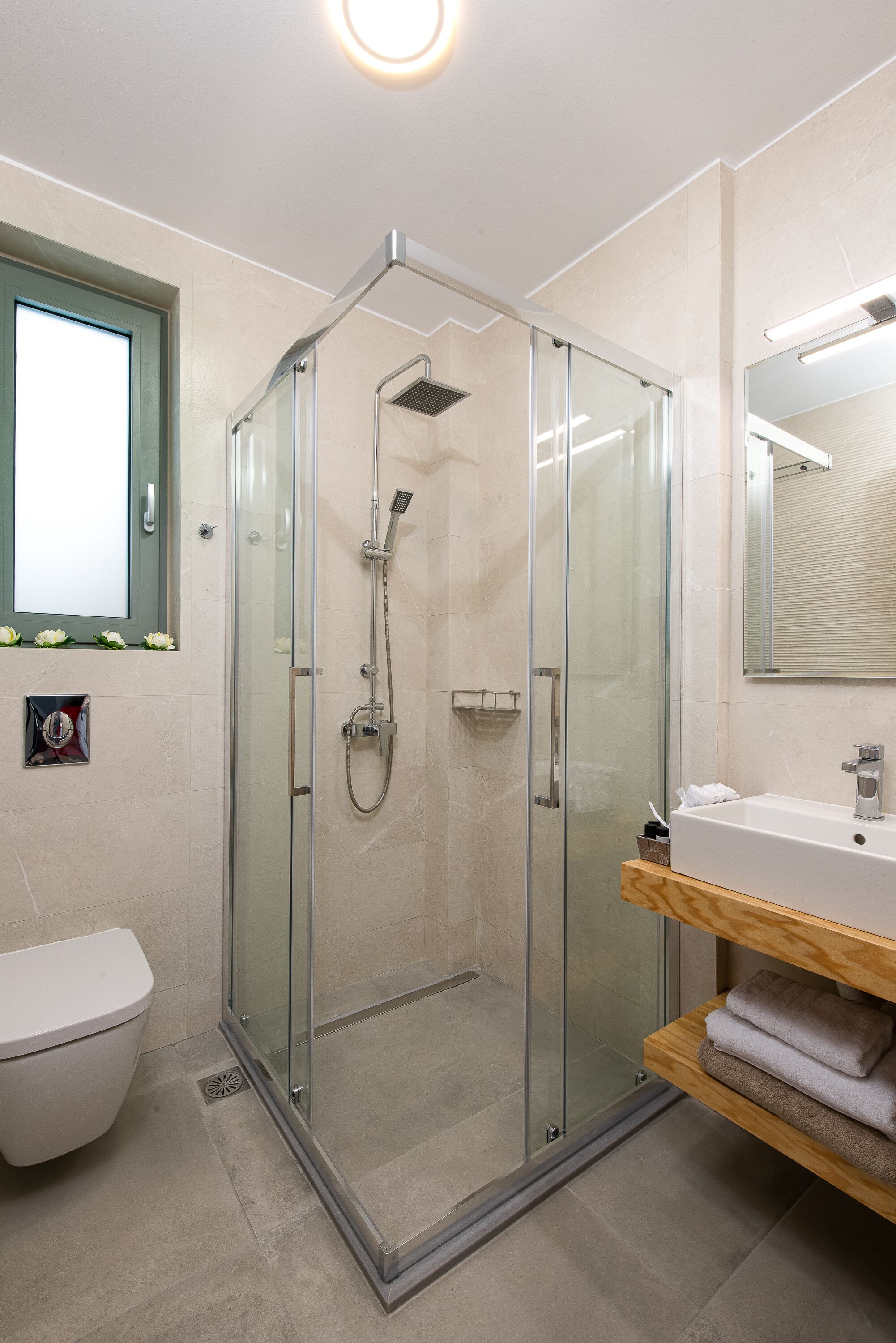A modern bathroom with a glass-enclosed shower, a white toilet, and a wooden vanity with a sink and towel rack.