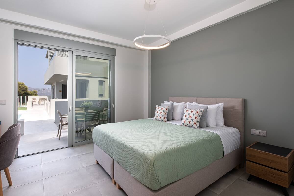 A modern bedroom with a large bed, a nightstand, and a sliding glass door leading to an outdoor area.