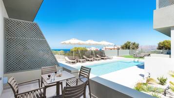 A poolside area with lounge chairs, umbrellas, and a table with chairs.