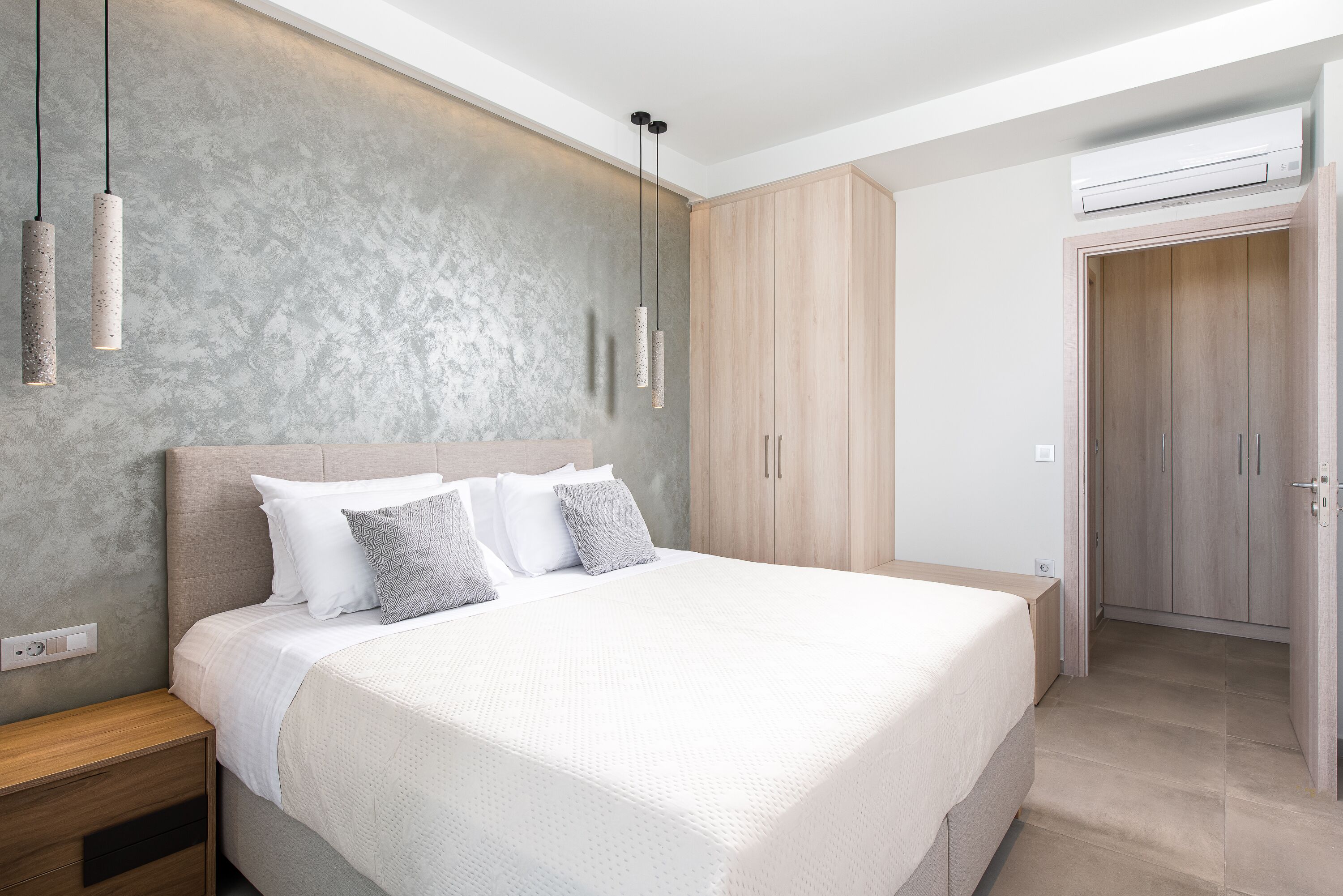 A modern bedroom with a large bed, wooden wardrobe, and pendant lights.