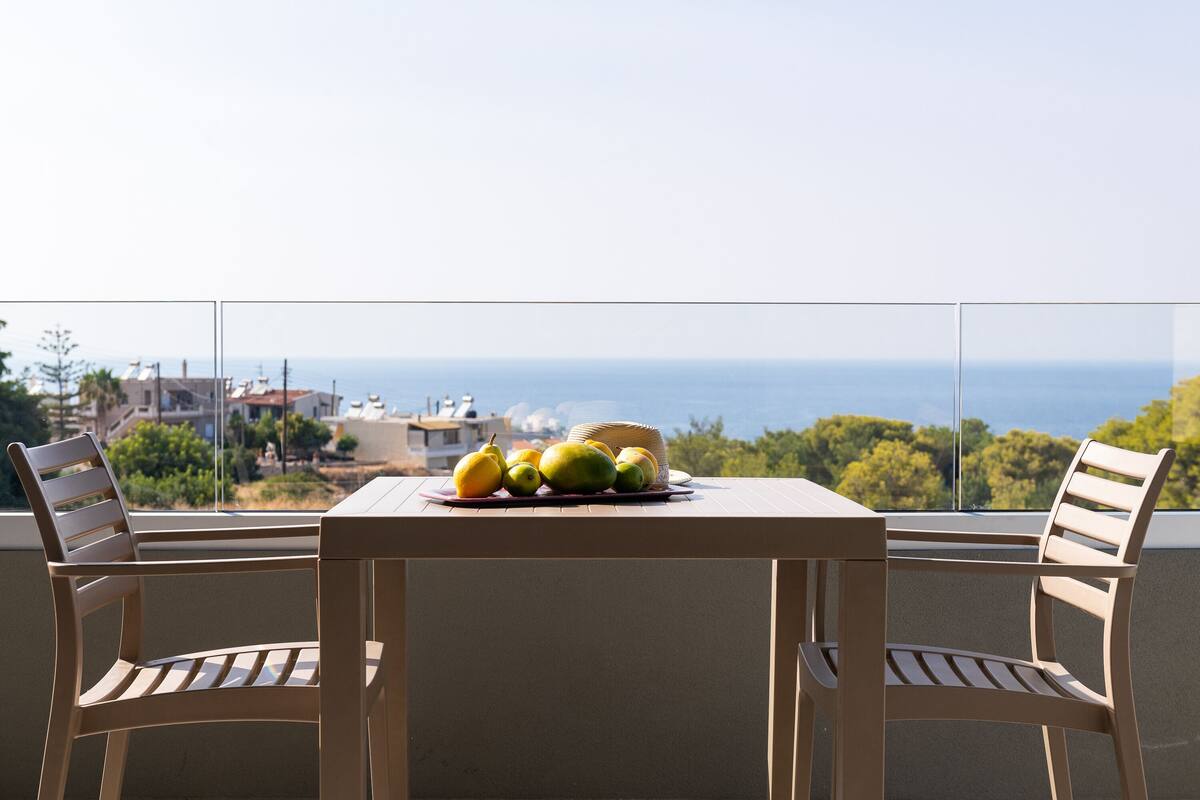 A balcony with a table set for two, featuring a fruit bowl and a wicker basket.
