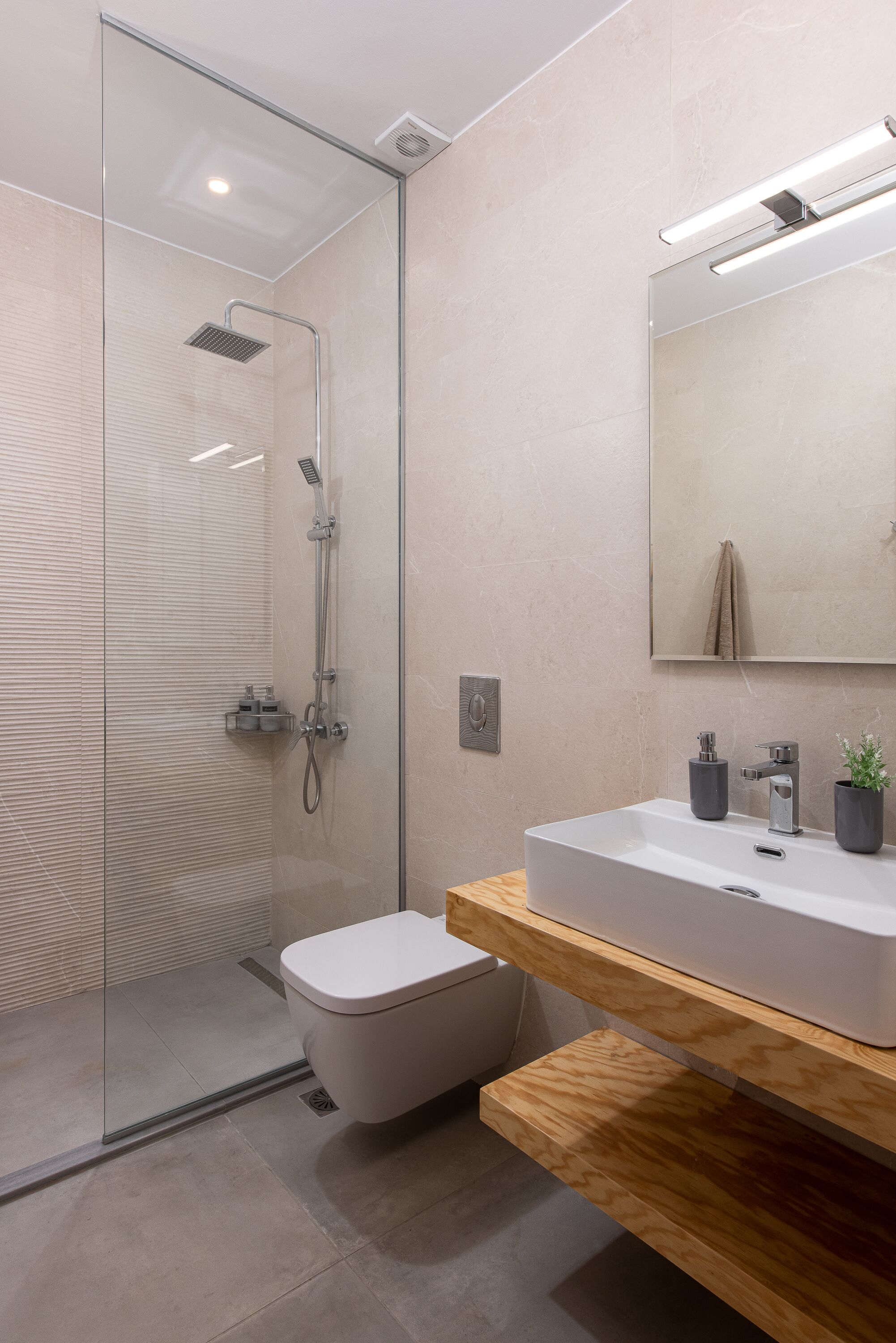 Un baño moderno con cabina de ducha de vidrio, inodoro blanco, tocador de madera con lavabo y espejo sobre el tocador.