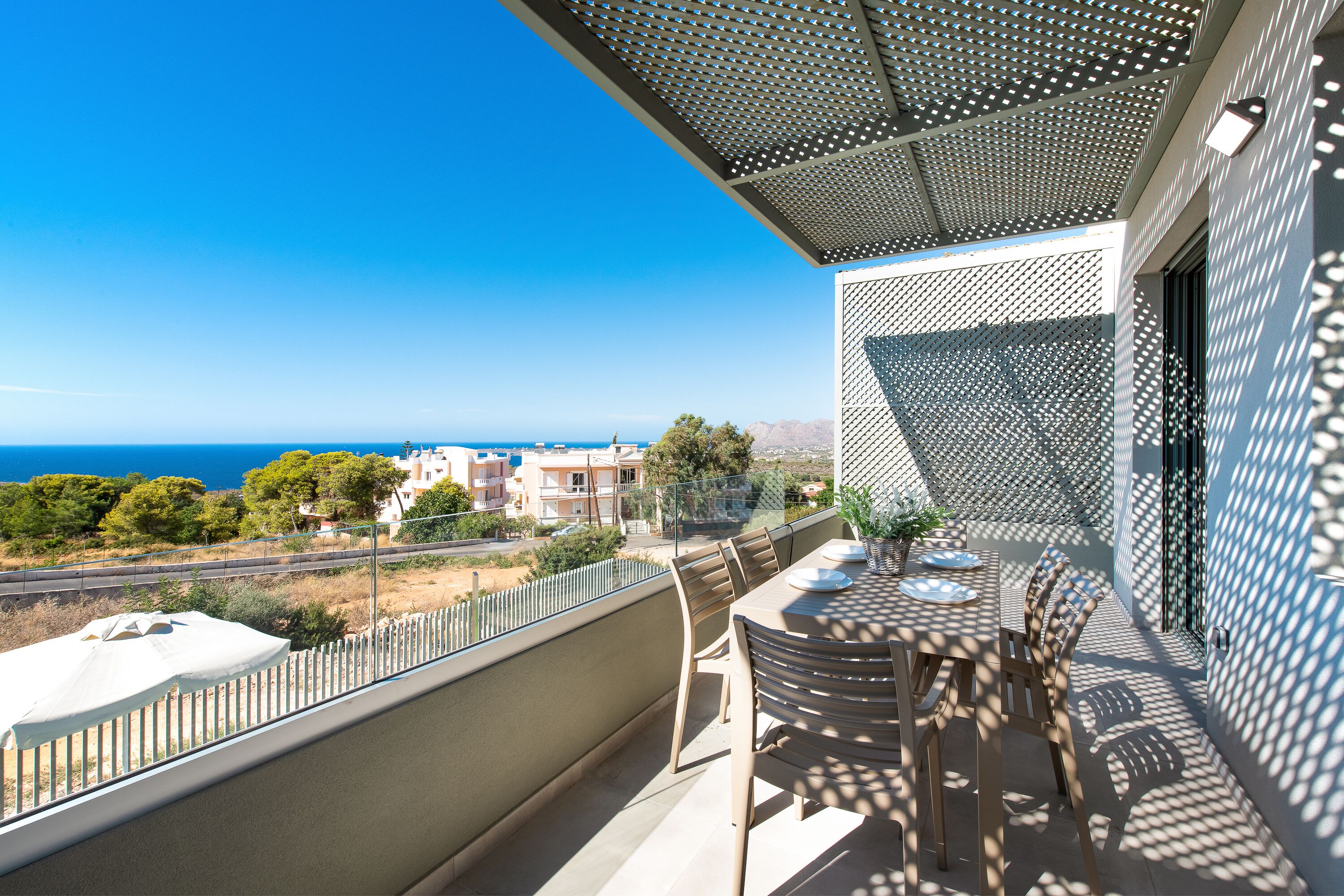 A balcony with a table and chairs, overlooking a coastal area with buildings and trees.