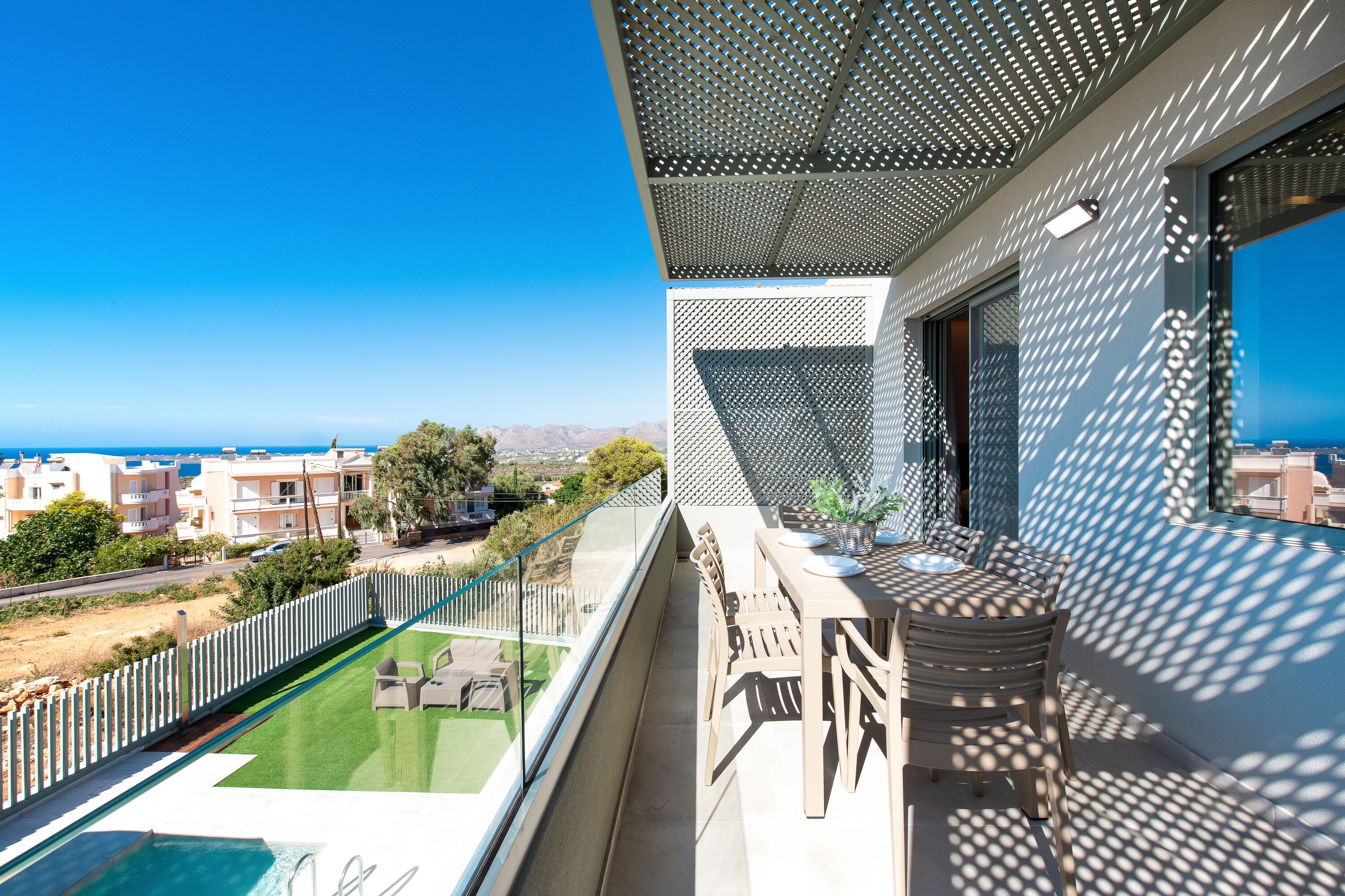 A balcony with a pool, outdoor furniture, and a view of the sea and neighboring buildings.